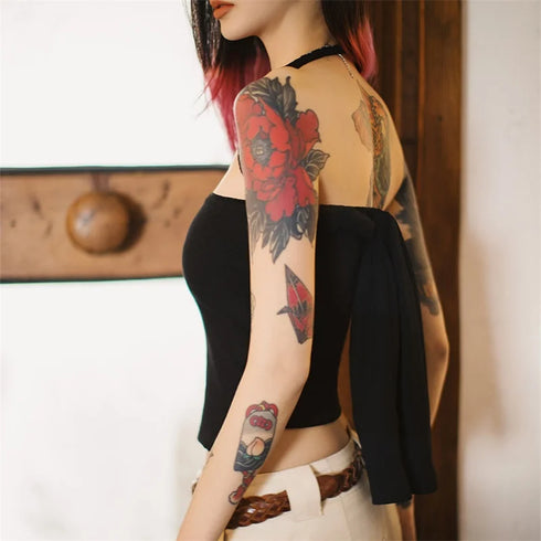 Person with tattoos on arms and back wearing a black top and white pants.